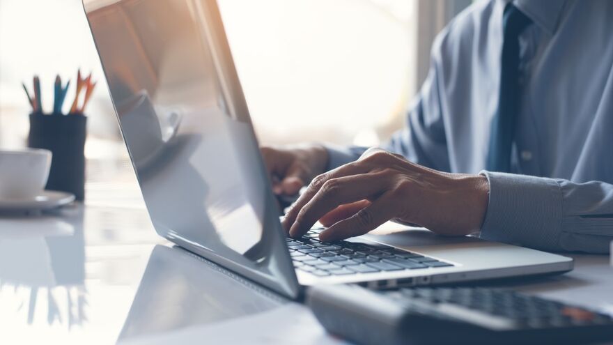 Man typing on laptop next to calculator 