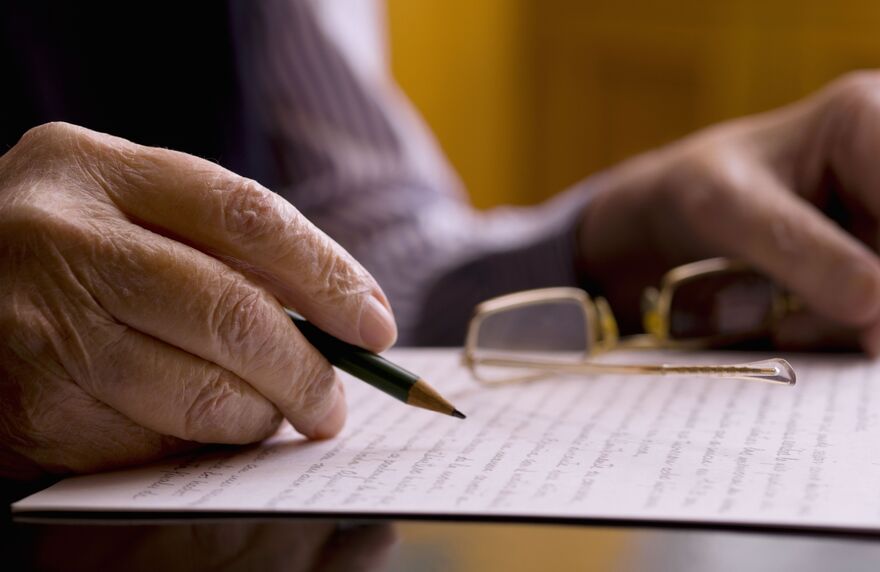 Close up of a hands of an old man, writing in a paper