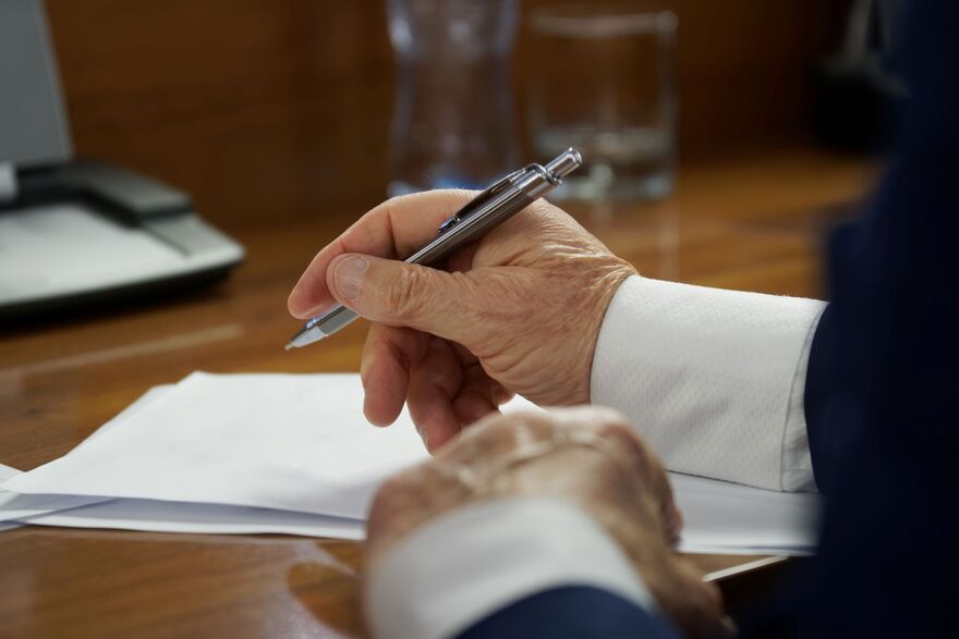 Elderly man in business suit, sitting at a table with pen