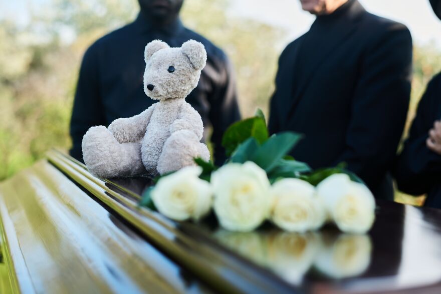 Focus on grey teddybear sitting on top of closed coffin 